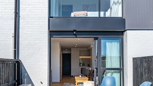 Een modern gebouw met twee verdiepingen, voorzien van een grote glazen deuropening, een klein buitenterrein met blauwe stoelen en een zichtbaar keuken.