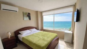 Una camera da letto con un letto, un comodino, una lampada, un quadro, una finestra vista oceano e un condizionatore d'aria.