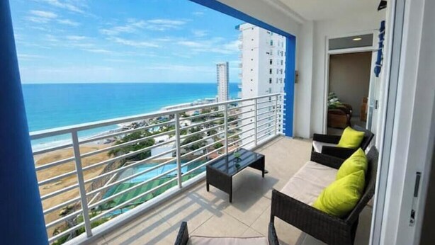 Un balcone con vista sull'oceano, un tavolino in vetro e due sedie in vimini con cuscini.