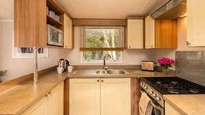 A compact kitchen with a sink, stove, and window with blinds. - 3BR Premium Caravan | Near Edinburgh |Parking|WiFi (Port Seton)