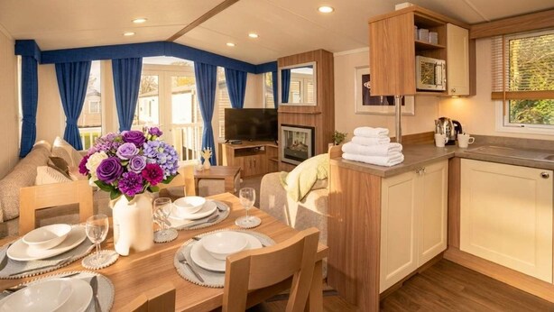 A cozy room with a dining table set for four, a TV, and a kitchen area with a microwave and sink. - 3BR Premium Caravan | Near Edinburgh |Parking|WiFi (Port Seton)