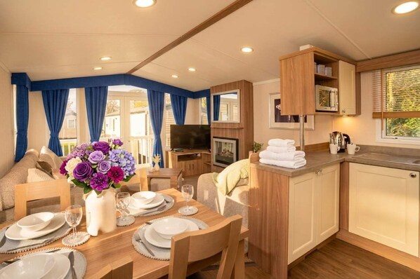 A cozy room with a dining table set for four, a TV, and a kitchen area with a microwave and sink.