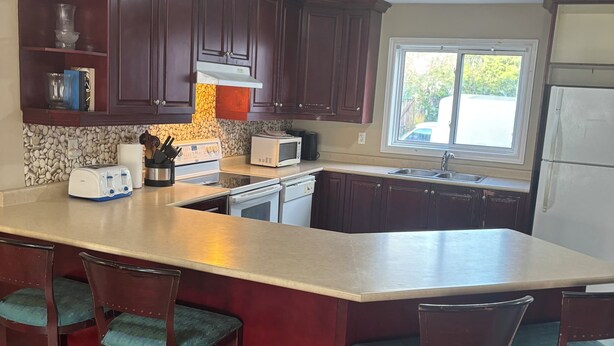 A kitchen with dark wooden cabinets, a large island with bar stools, a microwave, toaster, and a sink.