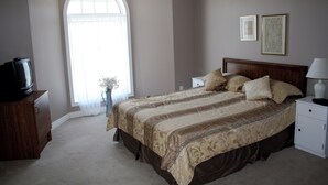 A bedroom with a large bed, a nightstand, a dresser, a television, and a window with curtains.