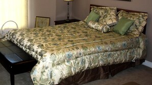 A bedroom with a bed, a nightstand, a lamp, a chair, and a framed picture on the wall.
