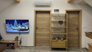 Een kamer met een televisie waarop een besneeuwd landschap te zien is, houten deuren, een plank met glazen en een witte airconditioner aan de muur.