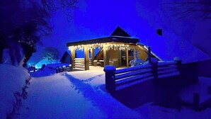 Een besneeuwde buitenruimte met een houten constructie, mogelijk een tuinhuisje, en een houten hek.
