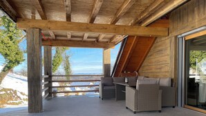 Een overdekt terras met rieten meubilair, uitzicht op besneeuwde bergen en een houten dakconstructie.