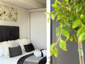 A bedroom with a bed, pillows, a headboard, a wall with a floral print, and a potted plant.