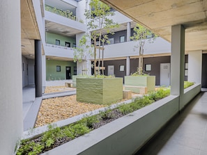 A multi-level building with numbered doors, a covered walkway, and planters with greenery.