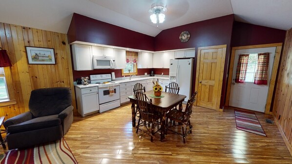 A compact kitchen with white cabinets, a microwave, and a stove. There is a dining table with chairs and a vase of flowers.