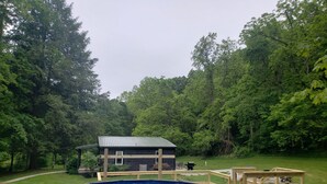 An outdoor swimming pool with a wooden deck and a small building in a wooded area.