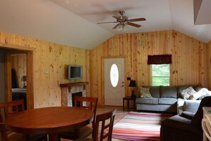 A wooden interior with a dining table, chairs, a sofa, a television, and a fireplace.