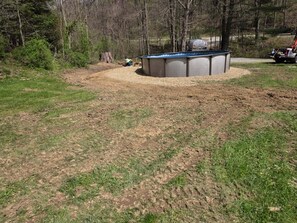 A circular pool with a surrounding gravel area, trees in the background, and a vehicle parked nearby.