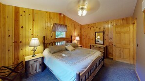 A wooden-paneled bedroom with a bed, bedside lamps, a chair, and a mirror.