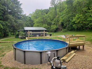 An above-ground swimming pool with a wooden deck and a house in the background.