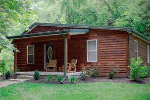 A wooden cabin with a porch, two windows, and a door.