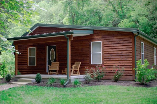 A wooden cabin with a porch, two windows, and a door.