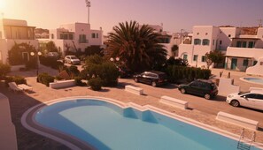 Ein Poolbereich mit klarem, blauem Pool, weißen Gebäuden mit grünen Fensterläden und geparkten Autos.