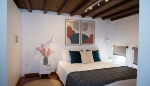 Ein Schlafzimmer mit Bett, Nachttischen, einer Blumenvase, abstrakter Wandkunst und einer Holzzahl.