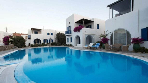 Une piscine avec des chaises longues et un bâtiment blanc agrémenté de touches de bleu.