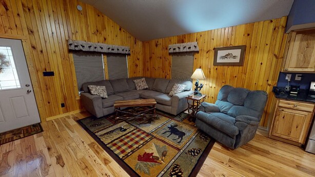 A cozy living room with a sectional sofa, a small table, a lamp, and a rug with animal prints. - Scotts Creek Cabins - Hilltop (Logan)