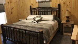 A wooden-paneled room with a bed, a nightstand, and a lamp. - Scotts Creek Cabins - Hilltop (Logan)