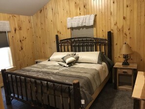 Ein Zimmer mit Holzwänden, einem Bett, einem Nachttisch und einer Lampe.