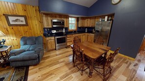 A kitchen with wooden cabinets, a dining table, and a gray sofa. - Scotts Creek Cabins - Hilltop (Logan)