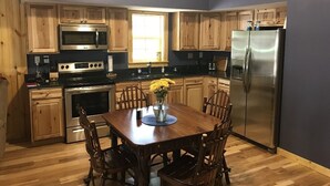 A kitchen with wooden cabinets, stainless steel appliances, a dining table with chairs, and a clock on the wall. - Scotts Creek Cabins - Hilltop (Logan)