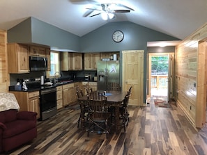 A kitchen with wooden cabinets, a dining table, chairs, a microwave, a refrigerator, and a ceiling fan. - Scotts Creek Cabins - Valleyview (Logan)