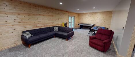 Una habitación con sofá modular, un sillón rojo, una mesa de billar y paredes de madera.