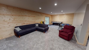 A room with a sectional sofa, a red armchair, a pool table, and wooden walls. - Scotts Creek Cabins - Valleyview (Logan)