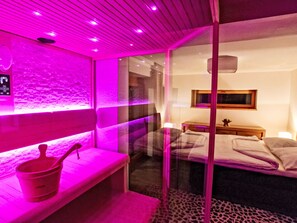 Um quarto com uma cama, um banco, um balde e um painel de vidro.