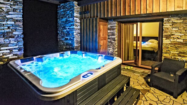 A hot tub in a stone-walled room with a wooden ceiling and a bed visible through a glass door. - Luxury Wellness by Interhome (Rokytnice nad Jizerou)