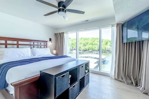 A hotel room with a bed, a ceiling fan, a TV, a large window, and a balcony.