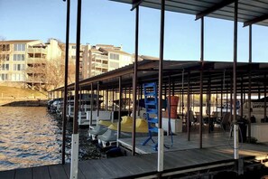 A covered dock area with boats, a water body, and buildings in the background.