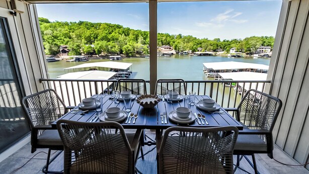 A dining area with a table set for four, overlooking a lake with boats and houses. - Sunset Lakefront Retreat with Luxe Upgrades (Osage Beach)