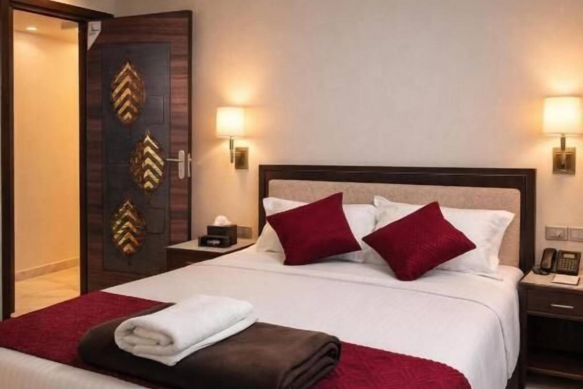 Ein Hotelzimmer mit einem großen Bett, einem Nachttisch, einer Lampe und einer Tür mit dekorativen Verzierungen.
