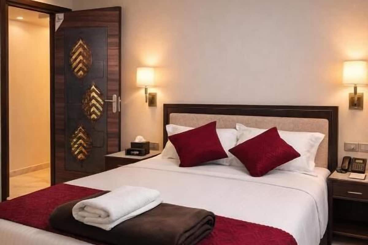 Una habitación de hotel con una cama grande, una mesita de noche, una lámpara y una puerta con paneles decorativos.