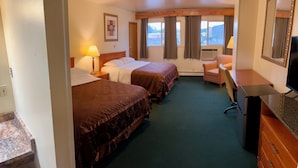 Et hotelværelse med to senge, et skrivebord, en stol, et fjernsyn og et vindue med gardiner.