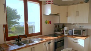 A kitchen with a window, stainless steel appliances, and white cabinets. - Panoramic Sea View Retreat in Brittany (Lampaul-Plouarzel)