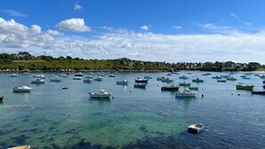 A coastal scene with numerous boats anchored in clear blue water, surrounded by greenery and a distant shoreline with buildings. - Panoramic Sea View Retreat in Brittany (Lampaul-Plouarzel)