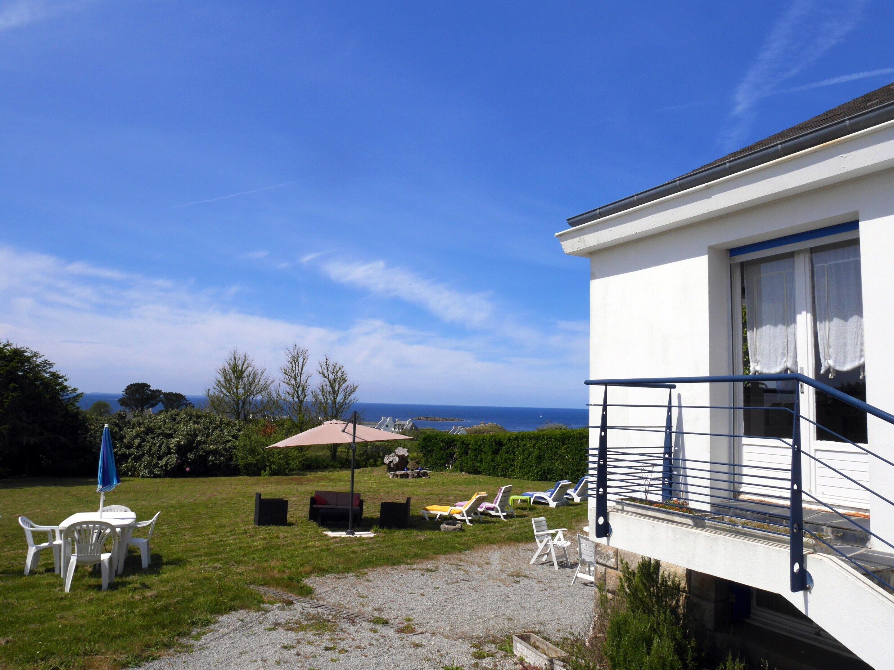 A white building with a balcony, outdoor seating, and a view of the sea.