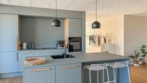Et moderne køkken med grå skabe, en central ø med barstole, kaffemaskine og et indbygget ovn.