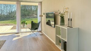 En moderne stue med en skydedør til en have, en grøn stol, et hvidt konsolbord med vase og stearinlys, samt et stort billede i ramme på væggen.