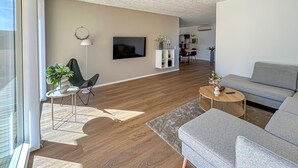 En moderne stue med sofa, sofabord, fjernsyn og reol.