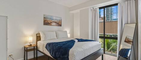 A bedroom with a bed, bedside lamp, a painting, a window with curtains, and a mirror.