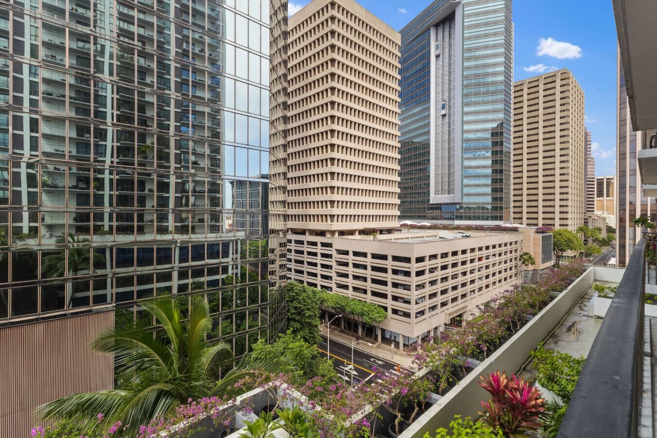 A modern urban building complex with high-rise structures, a central courtyard with greenery, and a clear sky.