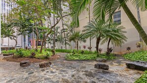 A courtyard with stone flooring, palm trees, and various plants. - Downtown Honolulu Condo | AC • W/D • Parking (Honolulu)